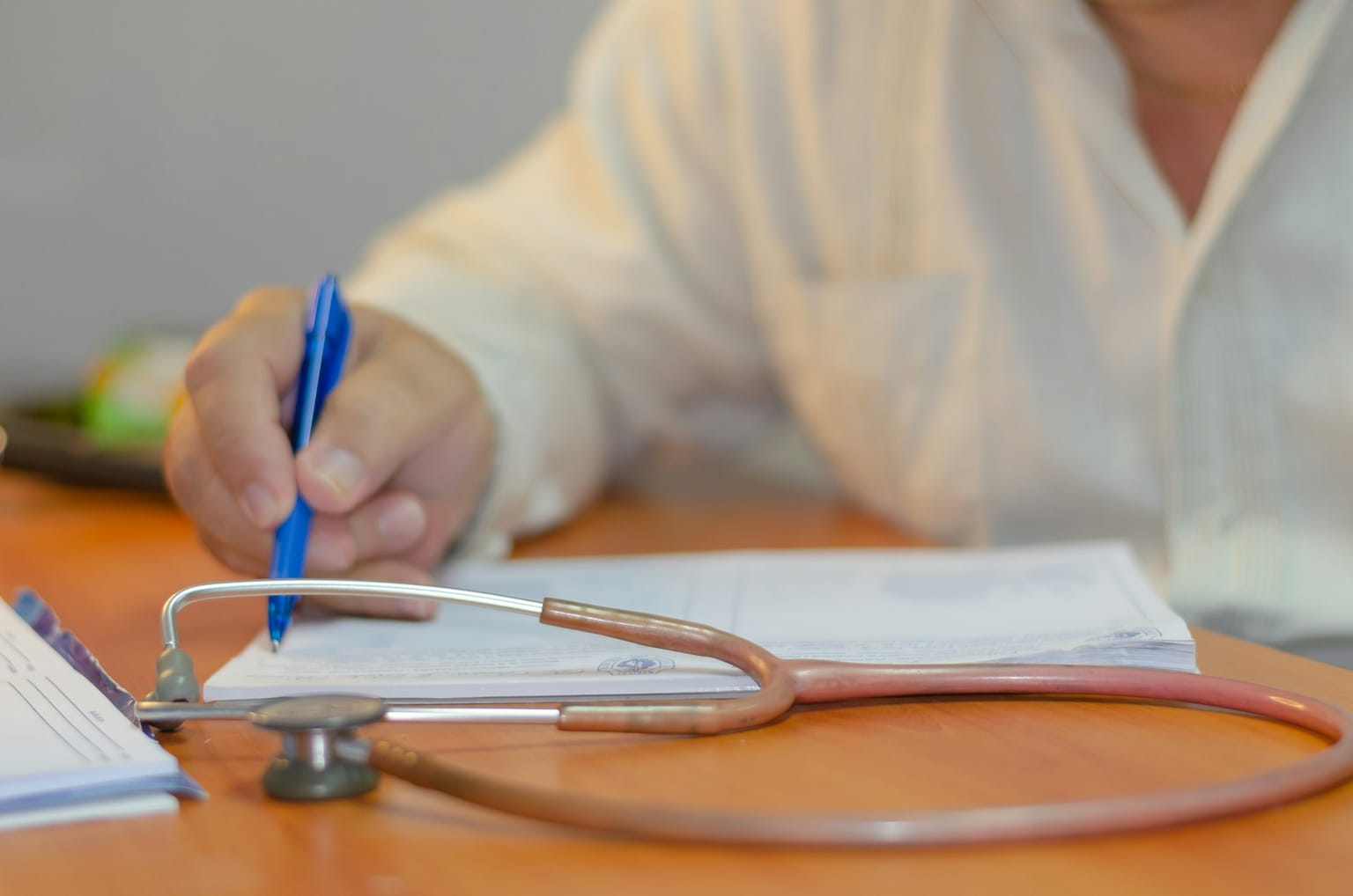 A doctor writing on a medical form next to a stethoscope